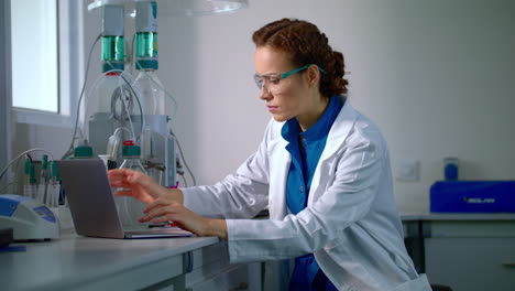Female-scientist-working-in-laboratory.-Lab-worker-typing-report-on-computer